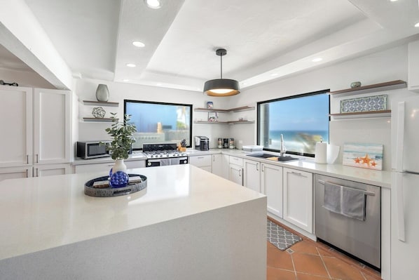 A serene morning in a sunlit, modern kitchen with a view of the ocean. 
