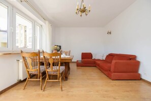 A spacious living room with light wooden floors, red armchairs, and table. The large bookshelf in the background adds warmth to the room.