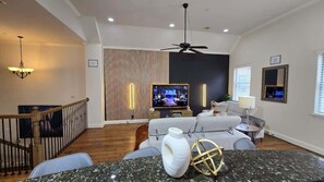 Elegantly designed, this living room features a sophisticated black accent wall with integrated wood paneling, highlighting the central 65-inch television. Ambient lighting enhances the wall's texture, providing a soft illumination. 