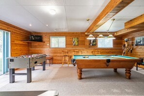 The downstairs/ground floor games room with a pool table, foosball table, air hockey, poker chips, board games & a TV with walkout access to the backyard's hot tub.