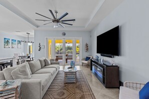 The living room features an oversized sofa, sitting chairs, an 85" smart TV, and an electric fireplace.