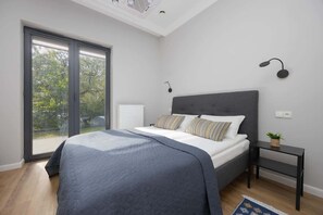 A modern bedroom with a large bed covered in gray bedding, next to a sliding door that opens to the outdoor patio, blending indoor comfort with outdoor access.