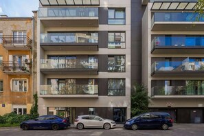 The exterior of the apartment building, showing a modern facade with balconies and a well-maintained courtyard and parking area.