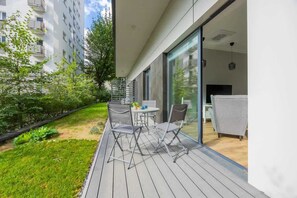 A spacious terrace with outdoor seating, featuring a table and chairs, overlooking a lush green space, perfect for relaxing in nature.