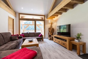 Relax in this comfortable living room featuring plush seating, a large flat-screen TV, and floor-to-ceiling windows that flood the space with natural light. A perfect spot to unwind and enjoy the scenic surroundings.