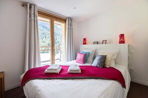 Rest peacefully in this cozy bedroom featuring a comfortable double bed with soft linens and vibrant red accents. Large windows offer plenty of natural light and serene views of the outdoors.