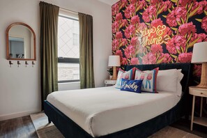 A bright and cheerful bedroom featuring a bold floral accent wall, fun decorative pillows, and a neon 'Rise & Shine' sign, creating a vibrant yet cozy atmosphere.