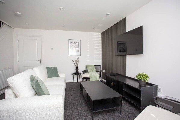 This living room features a bright and airy atmosphere, with its crisp white walls and matching white sofas that create a clean and elegant look as you sit right in front of the TV