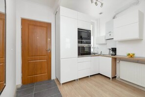 A modern kitchen with white cabinetry and built-in appliances. The flooring is grey, and the space has a clean, minimalist look.