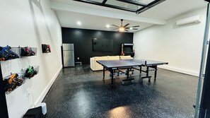 Game room in backyard with giant TV, ping pong, fridge, arcade, & more.