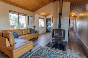 Relax in the cozy living area at Owl’s Nest Cabin, featuring a comfortable leather sectional, wood fired stove,  65" smart tv,  and incredible panoramic views of the valley and mountains.