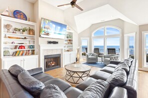 The bright and open Living Area offers cathedral ceilings, floor-to-ceiling windows, a wall-mounted flat-screen TV, and a gas fireplace for cozy evenings in the off-season.