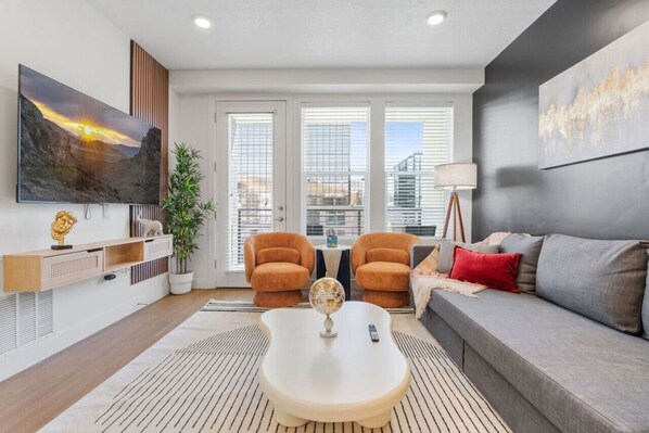 Relax in our cozy living room with plush sofas, a TV, and natural light streaming through large windows.