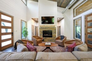 Spacious modern cabin living room with cozy fireplace, smart TV, comfy seating, and rustic wood accents. Perfect for family gatherings and relaxing in a forest retreat.