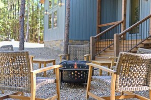 Outdoor fire pit seating area with woven chairs at cozy forest cabin retreat. Perfect for relaxing evenings, surrounded by trees and nature near a rustic wooden deck and stairs.