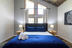 Cozy cabin bedroom with vaulted ceilings, stylish wood accents, modern decor, large windows, and plush bedding. Ideal forest getaway with comfort and natural light.