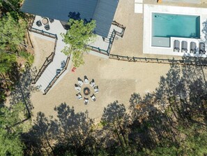 Overhead view of fire pit circle and expansive outdoor deck next to a modern pool in a forest setting.