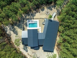 Aerial view of a luxury cabin surrounded by pine forest with private pool, fire pit, and open layout.