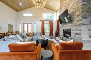 Modern living room with stone fireplace, orange chairs, and cozy sectional under a vaulted wood ceiling.