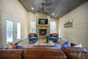 Living room with fireplace, TV, leather couch and forest views.