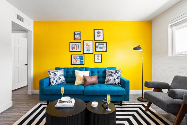 Bright and stylish living room featuring a vibrant yellow accent wall, cozy seating, and modern decor—perfect for relaxing or enjoying a movie on the Smart TV.
