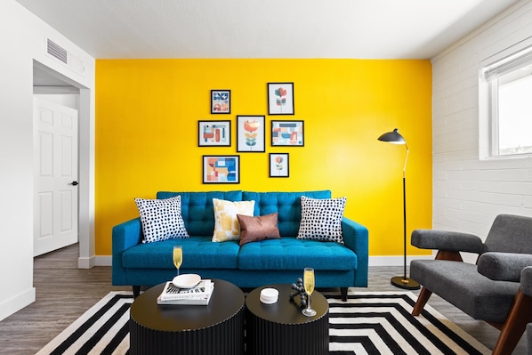 Bright and stylish living room featuring a vibrant yellow accent wall, cozy seating, and modern decor—perfect for relaxing or enjoying a movie on the Smart TV.