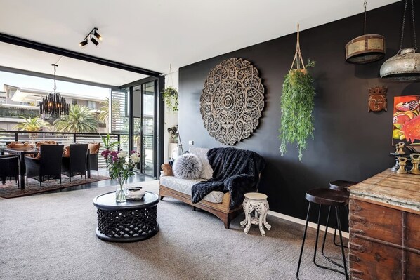 Step into the inviting living room, where bohemian elegance meets modern comfort. Relax on plush seating, surrounded by intricate wall art and lush greenery, creating a peaceful retreat after a day of exploring Sydney.
