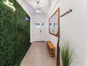 This chic entryway, adorned with lush faux foliage and modern neon signs