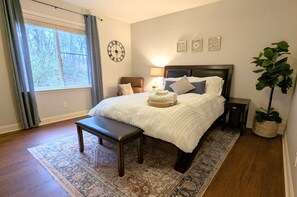 This bedroom has a queen bed, accent chair, smart TV. View of the wooded ravine.