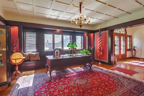 This office space has rich wood accents, a classic chandelier, and ample natural light, perfect for focused work or leisurely reading.