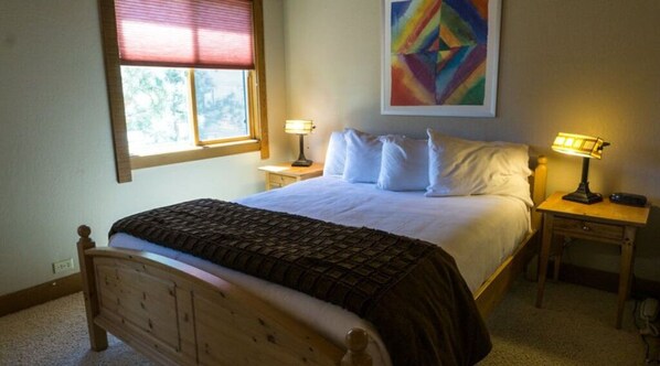 Bright and inviting bedroom featuring a comfortable bed, bedside lamps, and charming artwork.
