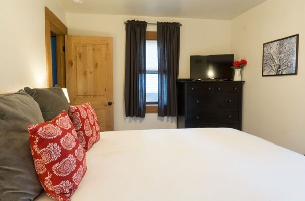 Cozy bedroom with rustic charm, featuring wooden furniture, a comfortable bed, and vibrant pillows for a touch of color.