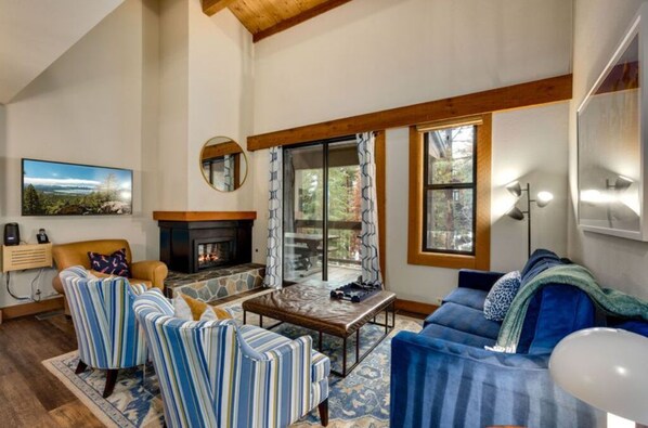 Inviting living area featuring high ceilings, a cozy fireplace, and comfortable seating, perfect for relaxing and socializing.