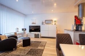Beach House 21 – Großzügiger Wohnraum mit TV, Küche und gemütlicher Sitzecke im Tageslicht.