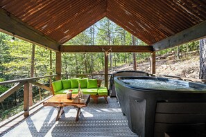 Forest-side deck with hot tub, green sofa, and cozy wooden accents.
