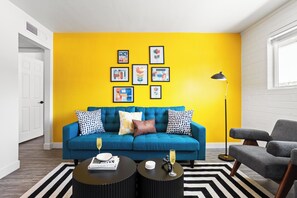 Unit 1: Bright and stylish living room featuring a vibrant yellow accent wall, cozy seating, and modern decor—perfect for relaxing or enjoying a movie on the Smart TV.