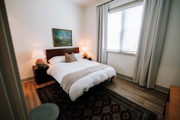 Relax in our cozy bedroom, featuring a blend of modern design elements and natural light from the large windows. The inviting decor, including beautiful wall art decor, creates a serene atmosphere perfect for relaxation.