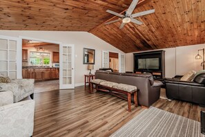 Spacious living area with vaulted wood ceilings, cozy seating, and French doors leading to a bright kitchen—ideal for relaxation and entertaining.