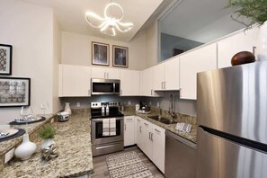 Modern kitchen with sleek granite countertops, stainless steel appliances, and stylish pendant lighting. The open layout offers a bright, contemporary feel, perfect for preparing meals and entertaining. 