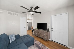 Living room showing entry door, Smart Samsung TV, Couch that converts to full sized bed, and look to kitchen/dining area