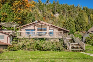 The cottage’s exterior is surrounded by lush greenery, offering a true escape into nature. The spacious deck is perfect for dining al fresco or enjoying morning coffee with a view of the lake.