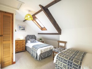 two single beds, throws and cushions.drawers, bedside lamp. chair. bedside table with plant.