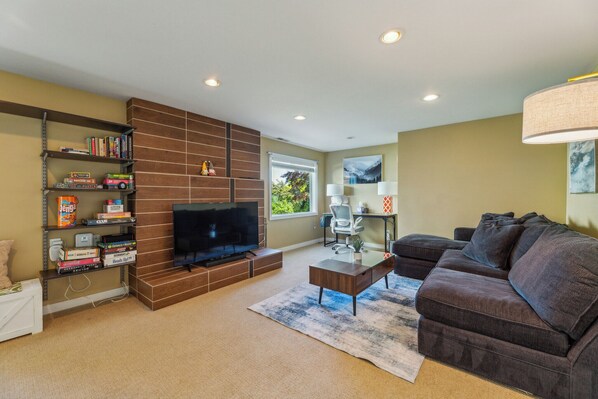 Large living room with a bright desk/ work area, and stocked with games.