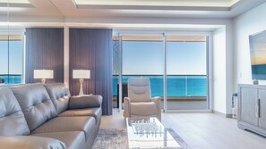 Enjoy a comfortable living room with large TV, leather sofa, and sunshine pouring in from the sliding glass doors that open onto the balcony.