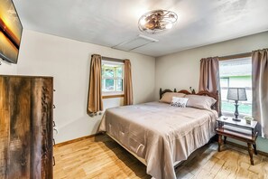 Comfortable bedroom with a cozy queen bed, wooden furniture, and a wall-mounted TV, offering a relaxing atmosphere.