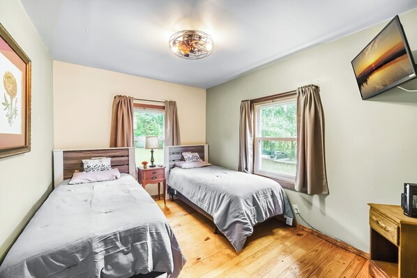 Bright bedroom with two twin beds, large windows, and a wall-mounted TV, offering a peaceful view of the outdoors.