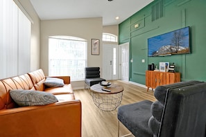 Relax in this chic living room, featuring a modern green accent wall, comfortable seating, and a smart TV. Perfect for cozy evenings or catching up on your favorite shows.