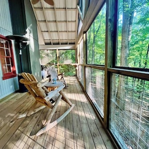 Fully screened in porch with wood log rocking chairs, grill, and heater.