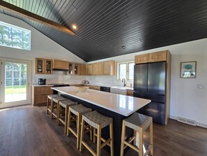 Modern lake house kitchen with sleek design. Features a spacious island with seating, stainless steel appliances, and ample storage. Enjoy the view from large windows, perfect for cooking while soaking in the serene surroundings.