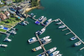 Aerial view of a marina with various boats docked, located adjacent to waterfront properties and lush green lawns.